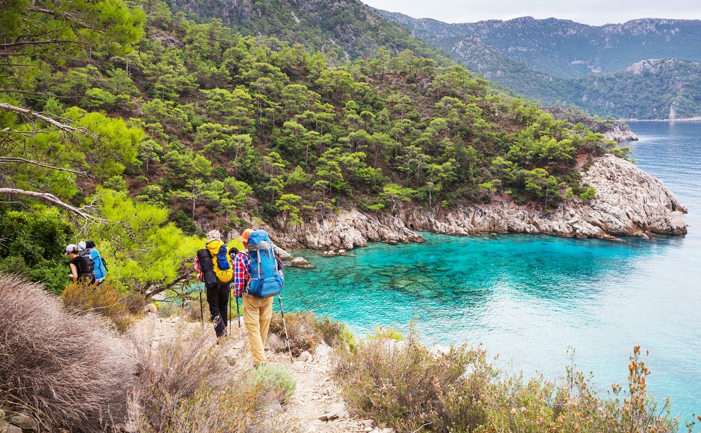 Hikers with backpacks descending the Lycian Way trail above a turquoise bay